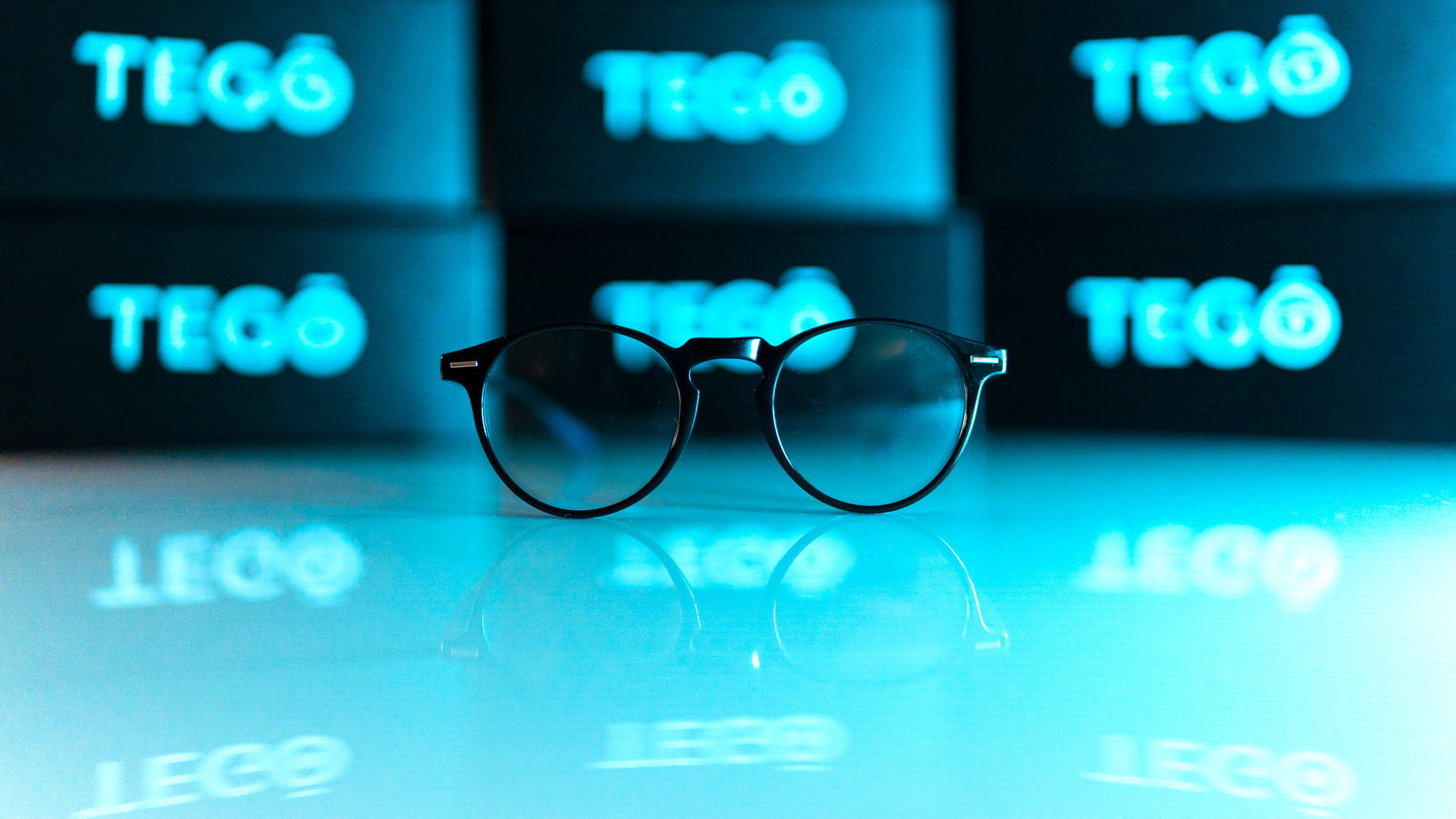 Sorte bluelight briller på en reflekterende overflade med TEGO kasser i baggrunden.
